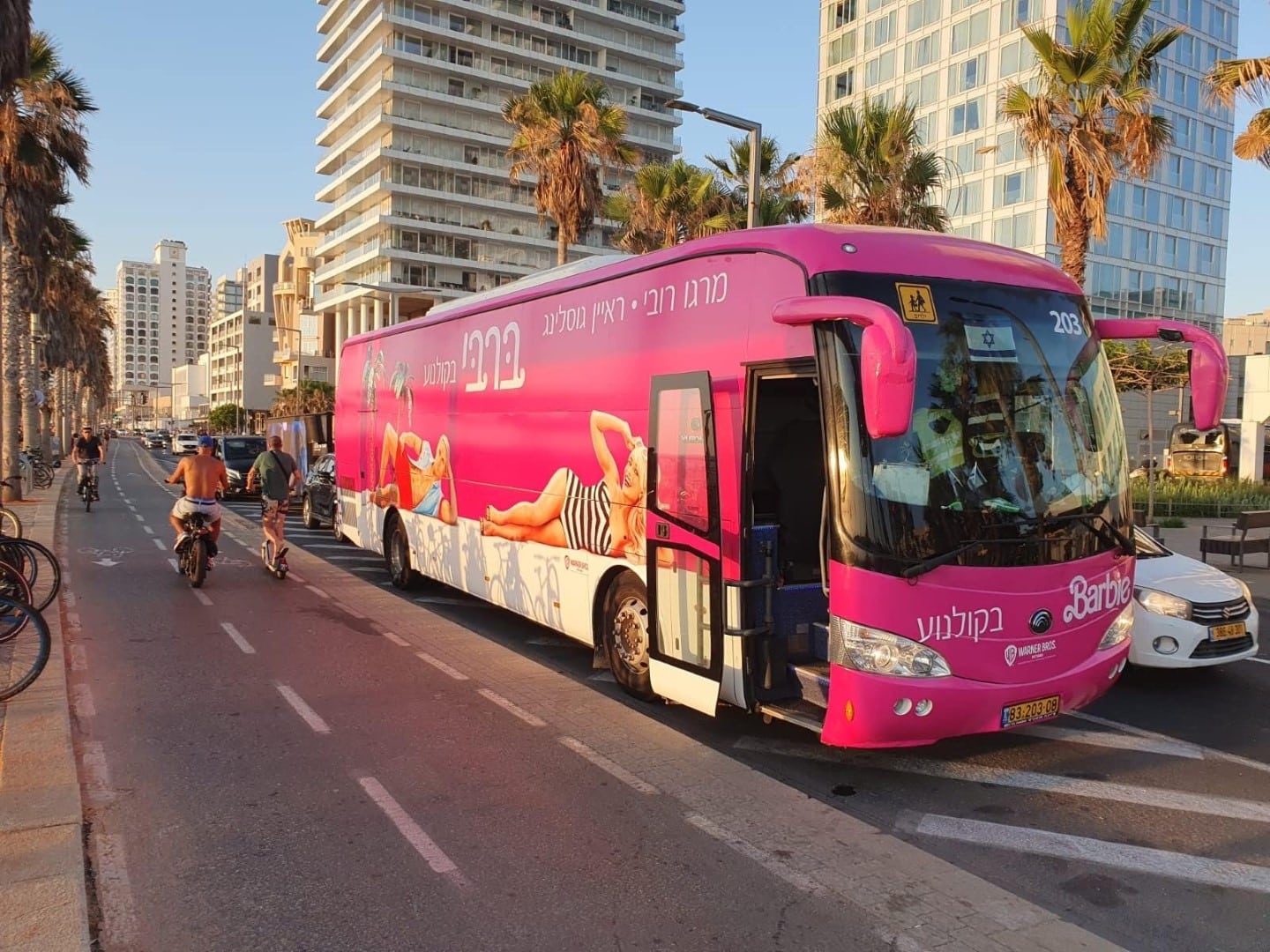 A pink bus is parked on a street in tel aviv. Barbie Poster is printed on the bus
