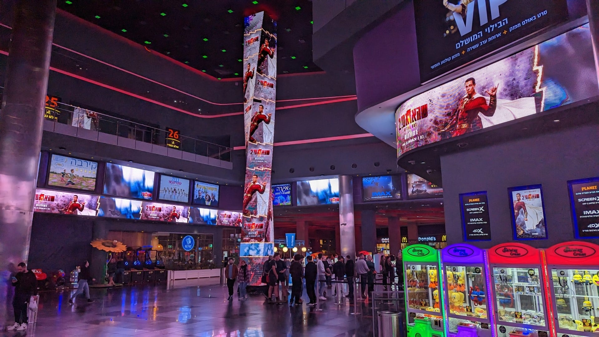 The inside of a movie theater with people walking around. Shazam Trailers is all over the screens